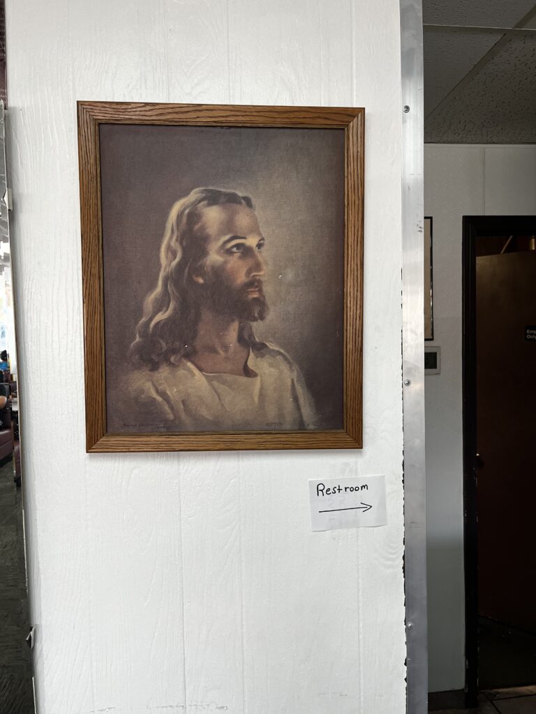Portrait of Jesus by Warner Sallman, and a scribbled sign pointing to the restroom just below